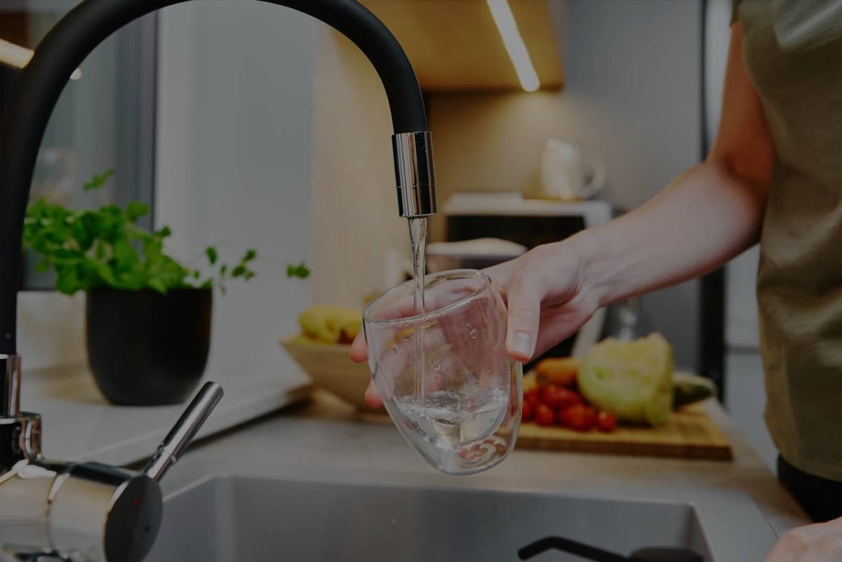 Person filling glass with clean filtered water in modern kitchen